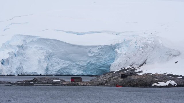 Port Lockroy Penguin Post Office on Antarctic Peninsula View From Cruise Ship. Large Glacier, Snow Behind Black and Red Building. A Small Tender Boat