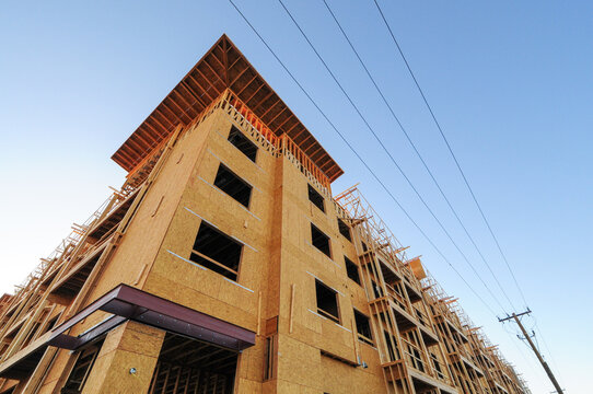Multistory apartment building under construction with wood framing and sheathing, illustrating multifamily housing development, residential construction, and urban growth