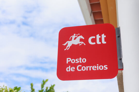 20260827 Alentejo, Portugal - CTT Posto de Correios sign outside a Portuguese post office, featuring the iconic red sign and horse rider logo against a blue sky.