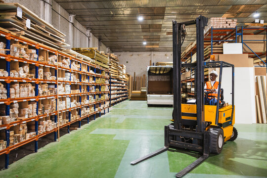 Worker driving forklift in lumberyard warehouse
