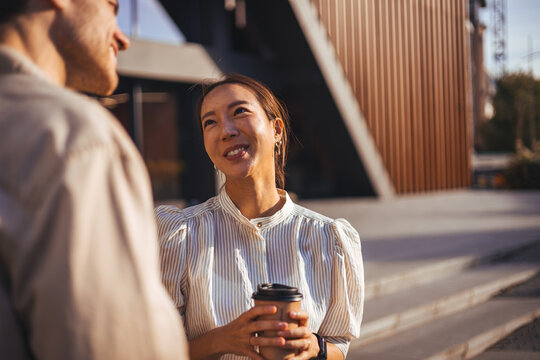Colleagues Sharing Coffee and Smiles During Casual Outdoor Conversation by Modern Office Building