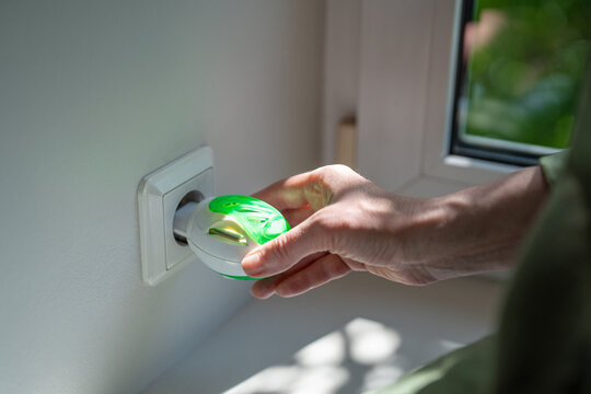 Woman adjusts electric fumigator containing mosquito repellent mat after plugging device into wall outlet, activating indoor insect protection against mosquitoes and prevent bites during summer.