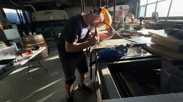 Skilled craftsman wearing a protective face shield using a specialized tool to bend and shape a metal piece with precision in his workshop
