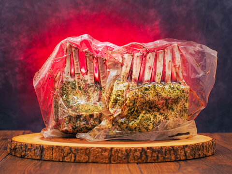 Two marinated rack of lamb in vacuum pack for extra freshness. Premium top quality lamb meat on wooden board and red hot background. Butcher craft and skill.