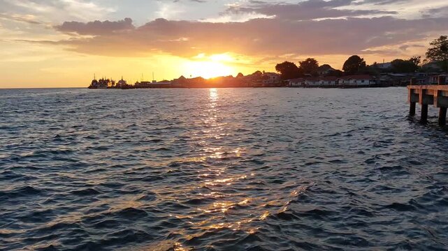 Vibrant sunset over coastal waters in Biak, Papua, Indonesia, with a wooden pier and village silhouette, highlighted by golden sun glints on gentle ocean ripples. Ideal for travel projects.