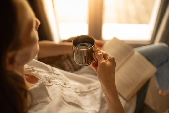 Woman Relaxing with Coffee and Book by Window in Warm Morning Light
