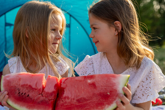 Young girls enjoying fresh watermelon while camping outdoors under sunny sky