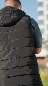Close up of man walking away from camera on outdoor path wearing black puffer vest over blue shirt and checkered flannel. focus remains steadily on his back as man moves forward