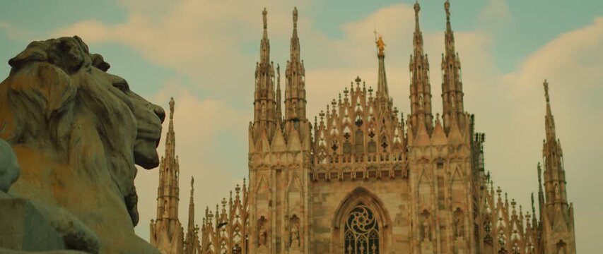 View of Milan Cathedral and lion statue against blue cloudy sky in summer Italy