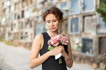 Fototapeta premium Visit to cemetery, woman in mourning clothes grieves for deceased relative. Near grave widow grieves and prays for soul of deceased relative, moment of remembrance, to pay tribute to memory
