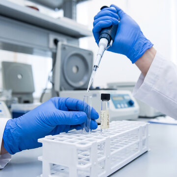 Gloved hands pipette a specimen into a test tube next to an already labeled tube in a lab rack