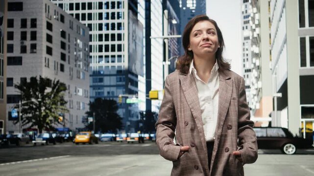 Smiling businesswoman stands on a city street with hands in blazer pockets; she looks at high-rise buildings and studies modern downtown architecture.