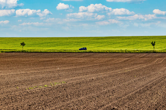 Plowed farmland with green fields and a car on a country road