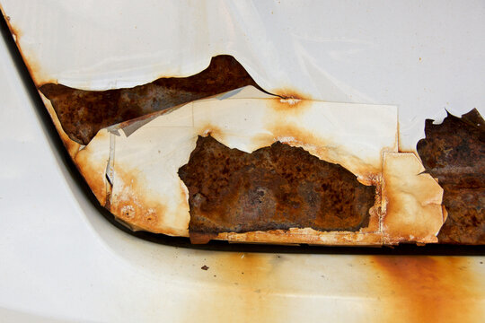 close up of rust on the trunk of a white car with peeling paint