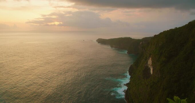 Sunset light illuminates the rugged cliffs and coastline of Nusa Penida Island