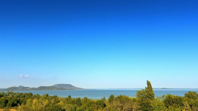 View of lake and hills during daytime. A clear view of a lake and distant hills under a blue sky during the daytime. Trees are seen in the foreground.