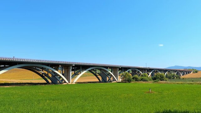 Bridge spans across green fields. A large bridge crosses over green fields on a clear sunny day. The area is peaceful with a blue sky above.