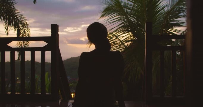 Woman sits quietly on a wooden terrace looking at the evening horizon in Nusa Penida