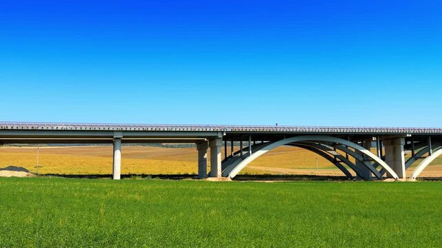Bridge over green field. A concrete bridge stands over a green field on a sunny day. The sky appears clear without clouds.