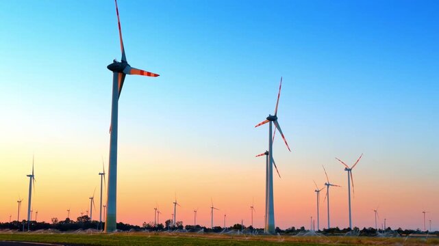 Wind turbines at sunset in a field. Wind turbines stand tall in a field as the sun sets. The sky shows shades of orange and blue.