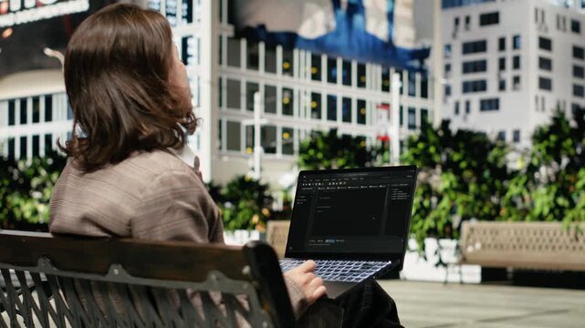 Programmer writing code on laptop while sitting on park bench