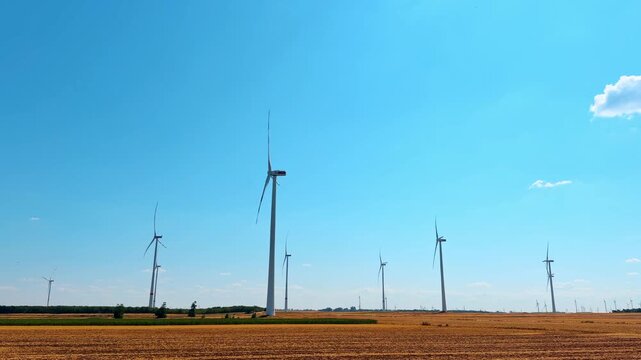 Wind turbines in harvested field under blue sky. Group of wind generators stands on stubble field beneath bright blue sky with light clouds.