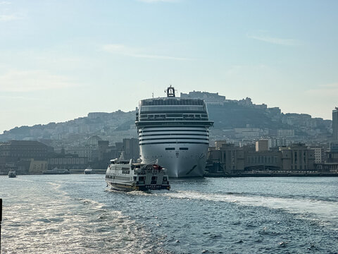 Naples, Italy - August 3, 2026. Ferry Boat Passing Giant MSC Cruise Ship in the Harbor of Naples. A wide, daytime shot captured from the water looking back at a local high-speed ferry boat ("Superjet"