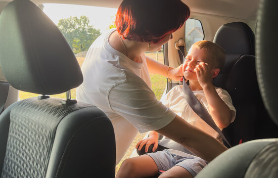Close up of a mother's hand fastening a safety seat belt for her toddler boy in a car seat. A parent ensuring child protection and road safety during a family trip.