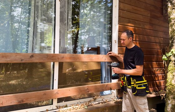 man on an extension ladder using a hammer to nail in new wood siding boards, homeowner maintenance and upkeep, making outdoor repairs on house 