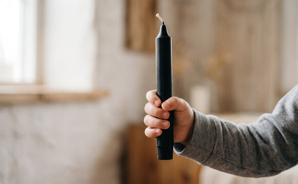 Child holding a black taper candle in hand close up, minimalist home decor and ritual concepts