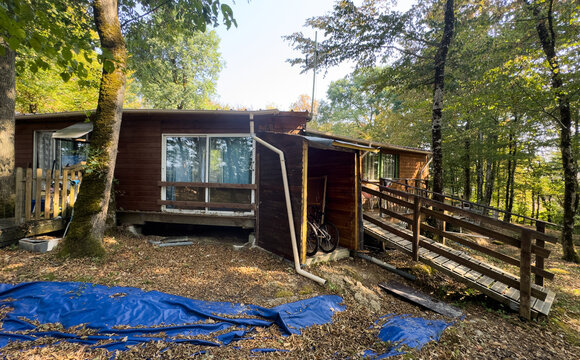 peaceful wooden cabin in forest with stationary bicycle and blue tarp on wooden deck, serene side view of real estate vacation rental in natural setting with brown and green tones.