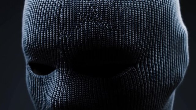 Knitted balaclava covers a persons face in a dark, shadowy closeup portrait