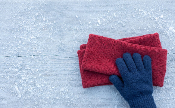 Red knitted scarf and blue glove on snowy wooden table background for winter cold weather concepts
