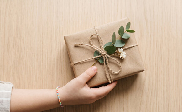 Child holding beautifully wrapped rustic gift box with craft paper and leaves for birthday celebration