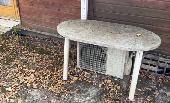 stationary concrete table with air conditioning unit on outdoor patio or garden area, neutral mood, ground-level perspective, gray and brown tones, for home improvement.