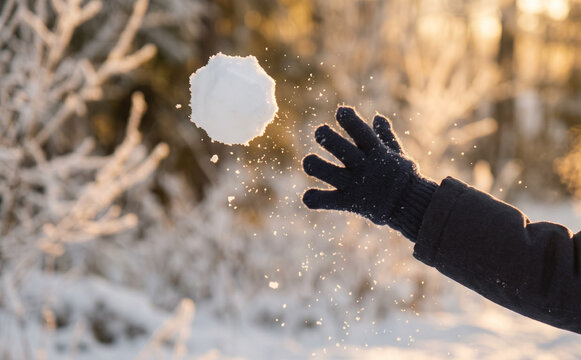 Person throwing a snowball outdoors in winter, close up on hand in glove with flying snow particles