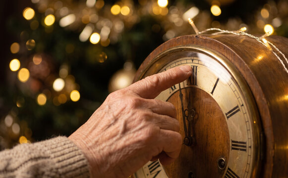 Elderly person hand pointing at midnight on a vintage wooden clock during Christmas eve celebration
