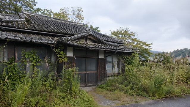 雑草に覆われて老朽化した瓦屋根の日本の古民家と空き家問題