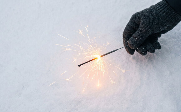 Sparkler in snow held by a gloved hand representing winter holidays, celebration, and magic