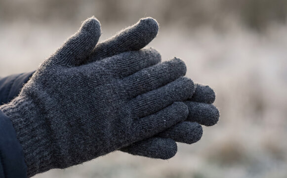 Person wearing warm knitted wool gloves rubbing hands together to stay warm in cold winter weather