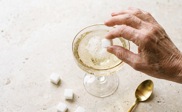 Elderly woman hand dropping sugar cube into champagne cocktail glass for preparation