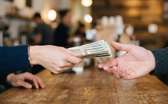 Woman paying cash with US dollar bills to a male cashier at a cafe counter, representing transaction and commerce