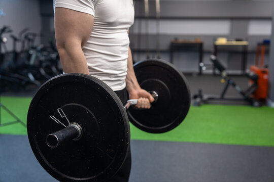 A muscular young man trains in the gym, doing barbell curls for biceps. Bodybuilding concept.