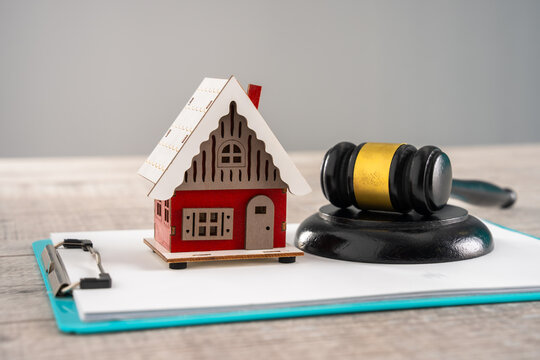 Wooden gavel on block near a model house on a wooden surface, representing a sale