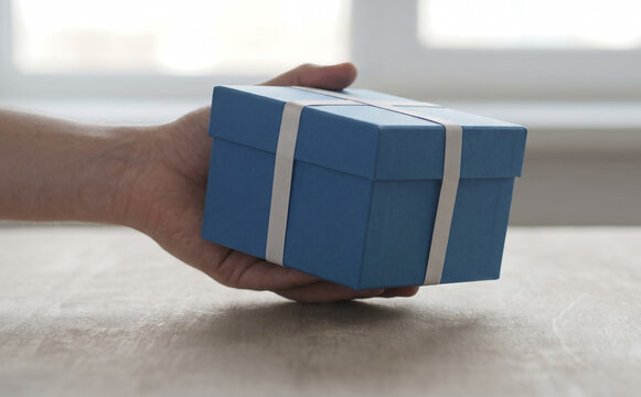 A person holding a blue gift box with white ribbon representing celebration and surprise