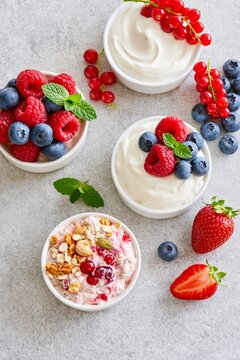 Assorted creamy yogurt bowls with fresh berries, mint and granola photographed from above