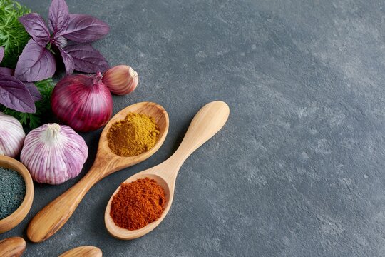 Colorful spices, garlic, onion and fresh herbs arranged on a dark stone background with copy space