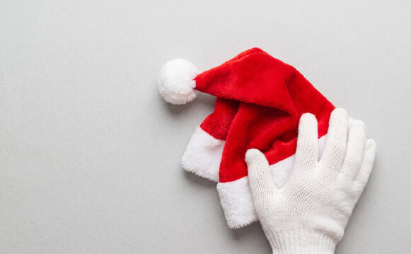 A hand in a white glove holding a Christmas Santa hat on a gray background for holiday concepts