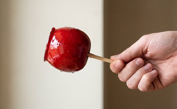 Hand holding a glossy red candy apple on a stick representing a sweet treat at a carnival fair