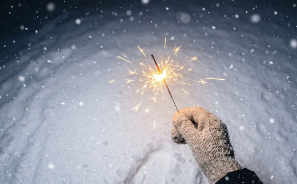 Gloved hand holding a burning sparkler outdoors in the snow during a winter night for celebration